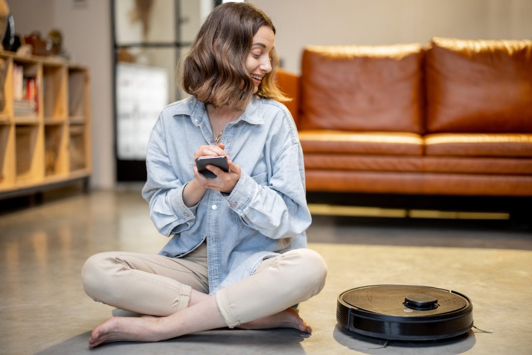 relaxed woman with phone and robotic vacuum cleaner 1